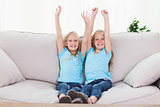 Twins raising their arms sitting on a couch