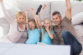 Cute twins and parents raising arms while watching television