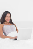 Cheerful woman using her laptop in bed