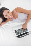 Attractive woman using her laptop lying in bed