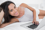 Cheerful woman using her laptop lying in bed