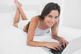 Pretty woman using her laptop lying in bed