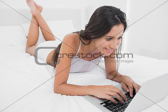 Happy woman using her laptop lying in bed