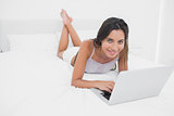 Portrait of a cheerful woman using her laptop lying in bed