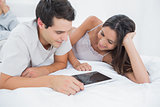 Couple using a tablet lying in bed