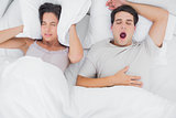 Woman covering ears with a pillow while her partner is snoring