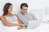 Couple using a laptop together lying in bed