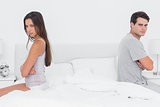 Couple sitting with their arms crossed back to back on bed