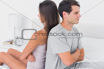 Couple sulking each other sitting back to back on bed