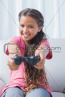 Smiling little girl playing video game on sofa