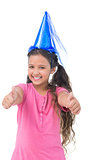 Smiling little girl wearing blue hat for a party and does thumbs up at camera