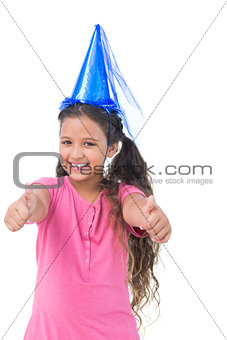 Smiling little girl wearing blue hat for a party and does thumbs up at camera