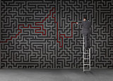 Businessman standing on a ladder and drawing a red line through black maze