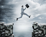 Businessman jumping a gap between cliffs