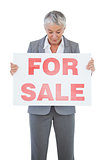 Estate agent holding and looking at sign for sale
