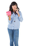 Thinking young woman holding her piggy bank