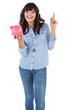 Smiling young woman with piggy bank pointing her finger