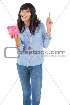Happy young woman with piggy bank pointing her finger