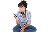 Young woman sitting on the floor with headphones holding her mobile phone