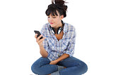 Smiling young woman sitting on the floor with headphones holding her mobile phone