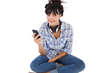 Happy young woman sitting on the floor with headphones holding her mobile phone