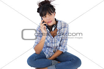 Brunette sitting on the floor with headphones calling someone