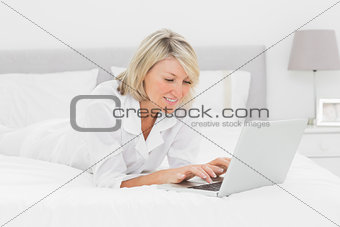 Smiling woman using her laptop on her bed