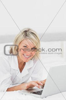 Happy woman using her laptop on her bed looking at camera
