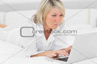 Happy woman using her laptop on her bed