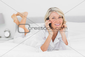 Happy woman making a phone call lying on bed