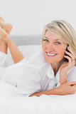 Blonde woman making a phone call lying on bed