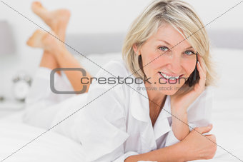 Cheerful woman making a phone call lying on bed