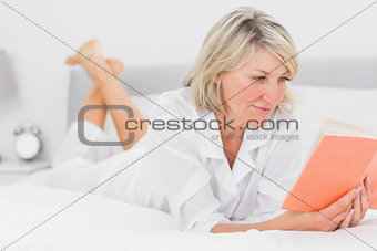 Cheerful woman reading a book lying on bed