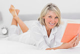 Happy woman reading a book lying on bed