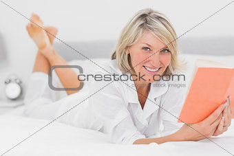 Happy woman reading a book lying on bed