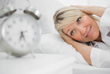 Blonde woman covering her ears from alarm clock noise