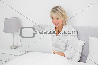 Happy woman sitting in bed with laptop