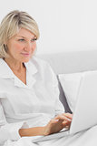 Cheerful woman sitting in bed with laptop