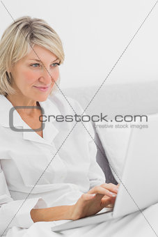 Cheerful woman sitting in bed with laptop