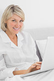 Cheerful woman sitting in bed with laptop looking at camera