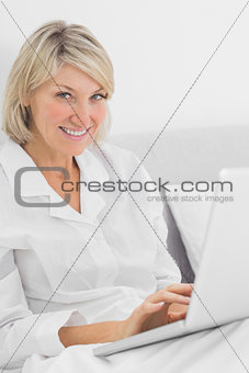 Cheerful woman sitting in bed with laptop looking at camera