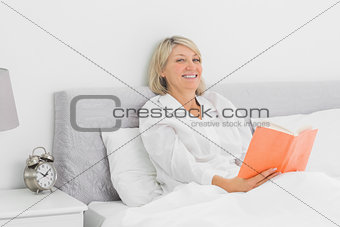Cheerful woman sitting in bed reading