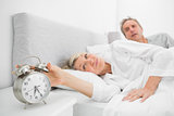 Woman in bed with partner turning off alarm clock