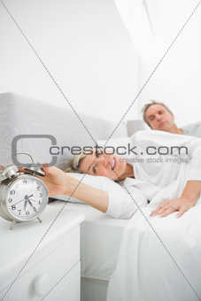 Blonde woman in bed with partner turning off alarm clock