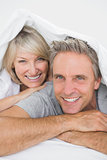 Couple smiling under the covers at the camera