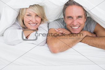Cheerful couple smiling under the covers at the camera