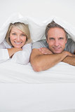 Attractive couple smiling under the covers at the camera