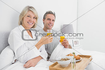 Happy couple having orange juice at breakfast in bed