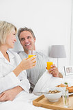 Smiling couple having orange juice at breakfast in bed