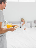 Man bringing breakfast in bed to his surprised partner